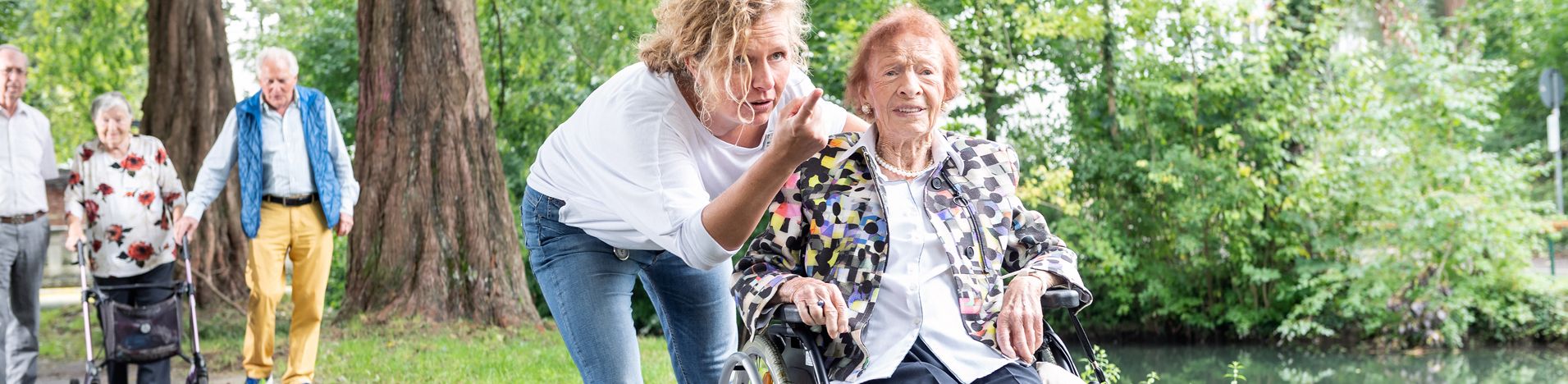 Pflegekraft zeigt der älteren Frau im Rollstuhl etwas im Park